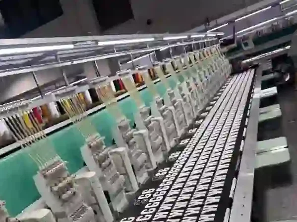 Multi-head industrial embroidery machine producing GG monogram patterns on black fabric