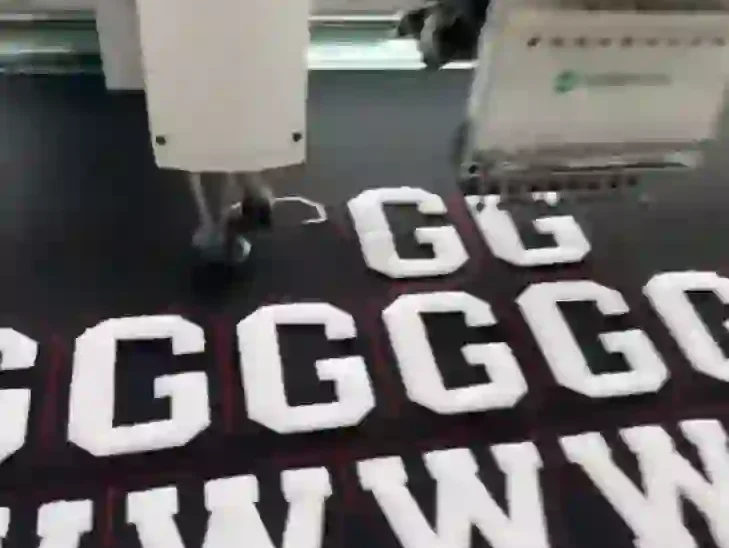 Embroidery machine working on white GG monogram letters on black fabric in close-up
