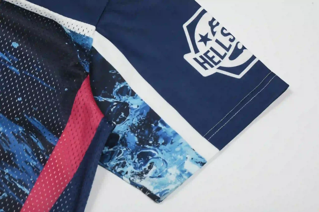 Close-up of the sleeve on a navy blue Hellstar mesh jersey, featuring the Hellstar shield logo on the cuff, a blue water-splash print, and red-and-blue perforated mesh panels