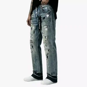 Purple Brand light wash distressed denim jeans with extensive rips, paint splatters, and a black hem, worn with white sneakers