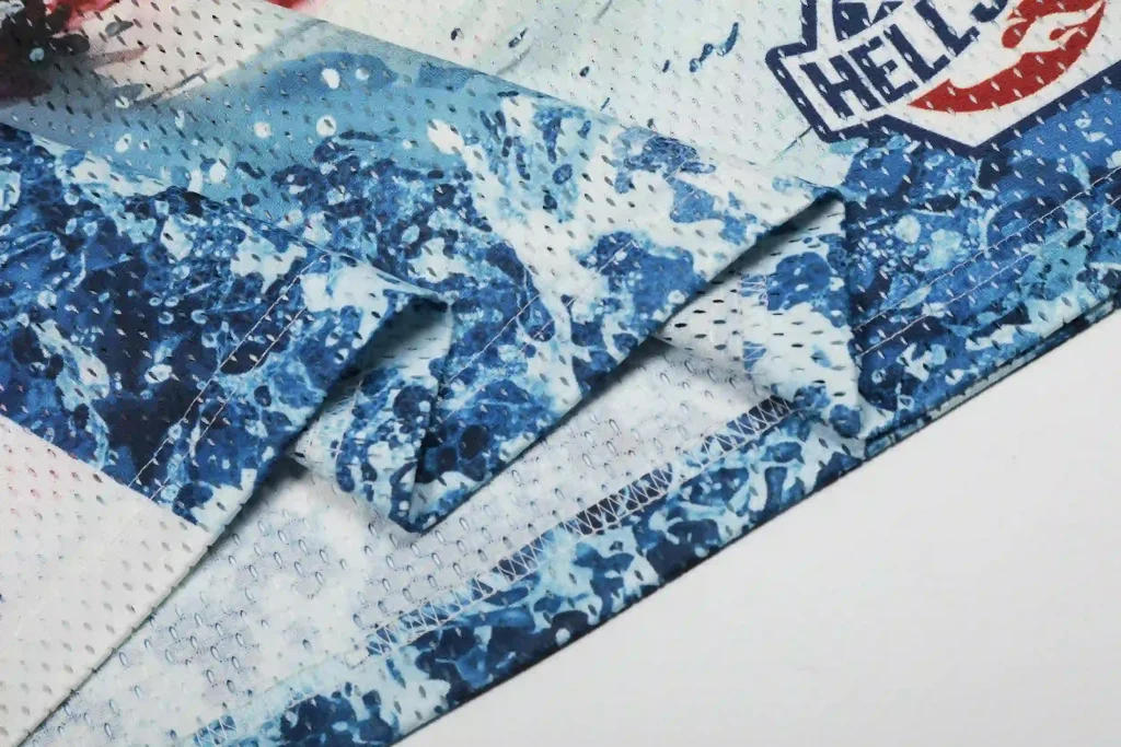 Close-up of the hem on a Hellstar mesh jersey, showcasing the blue water-splash print, reinforced stitching, and the Hellstar shield logo detail